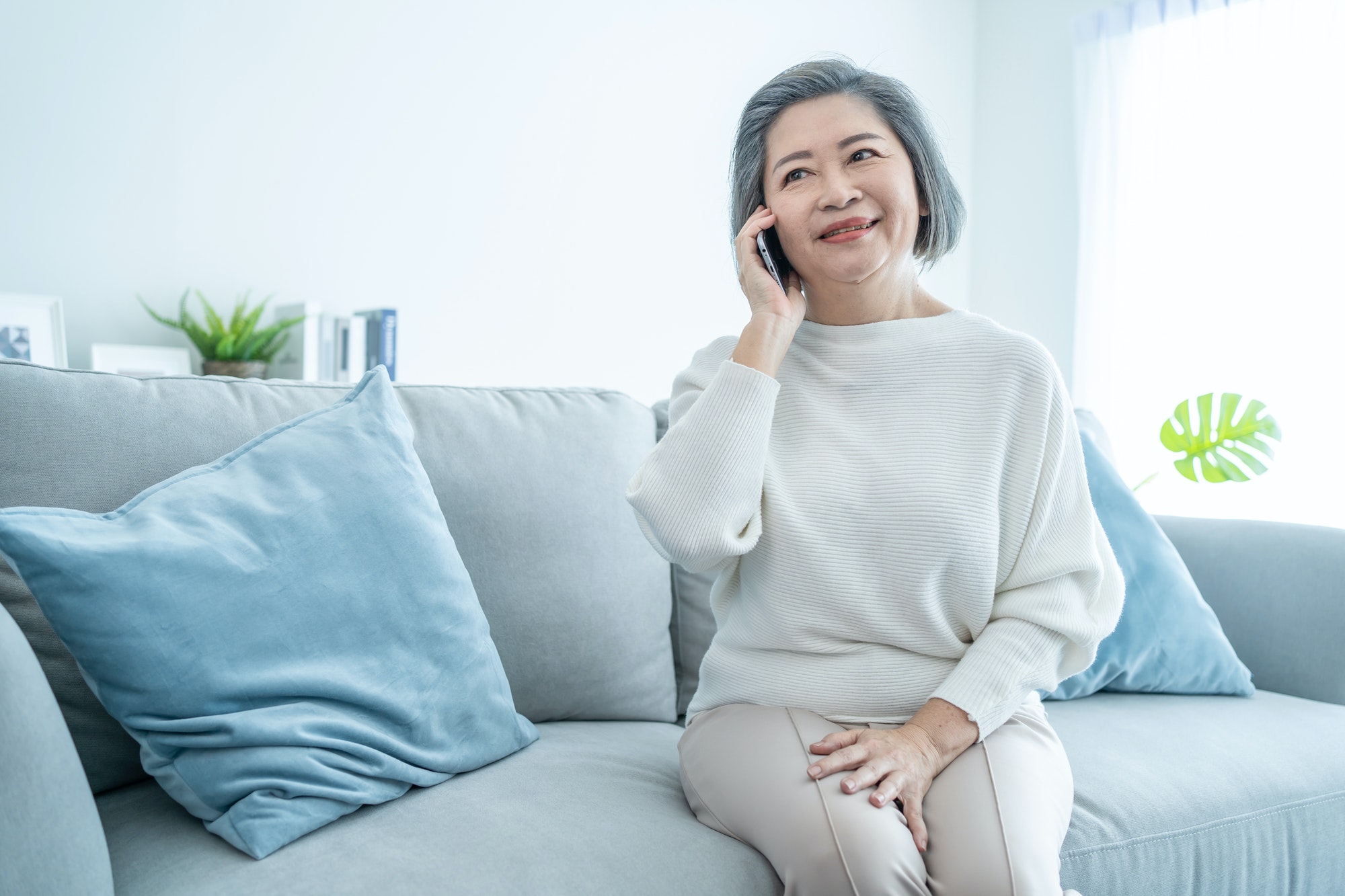 Asian senior elderly woman smile and talk on phone call in living room.